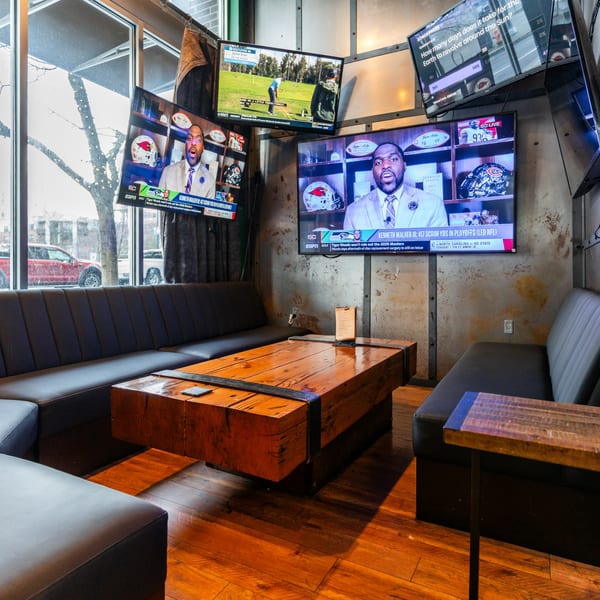 A cozy bar area with black leather booths, a large wooden table, and multiple TVs showing sports.