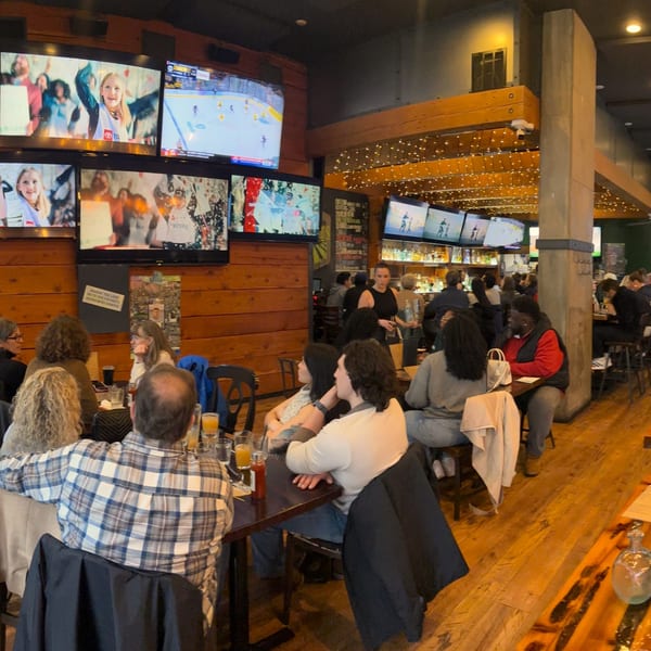 Diners and drinkers fill The Fields Bar & Grill, with multiple TVs showing sports and entertainment.