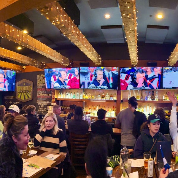 Patrons at The Fields Bar & Grill watching sports on multiple screens above a liquor bar.