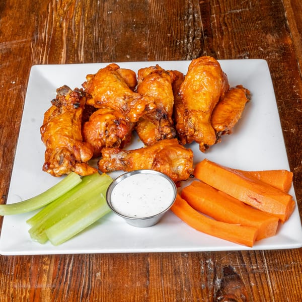 A plate of buffalo wings with celery sticks, carrot sticks, and a side of ranch dressing.