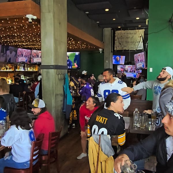 Patrons in sports jerseys watching games on multiple TVs at The Fields Bar & Grill.