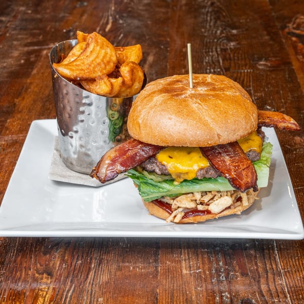 A bacon cheeseburger with lettuce, crispy onions, and a side of potato wedges on a white plate.