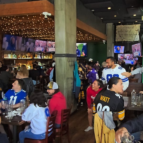 Patrons in sports jerseys watching games on multiple TVs at The Fields Bar & Grill.