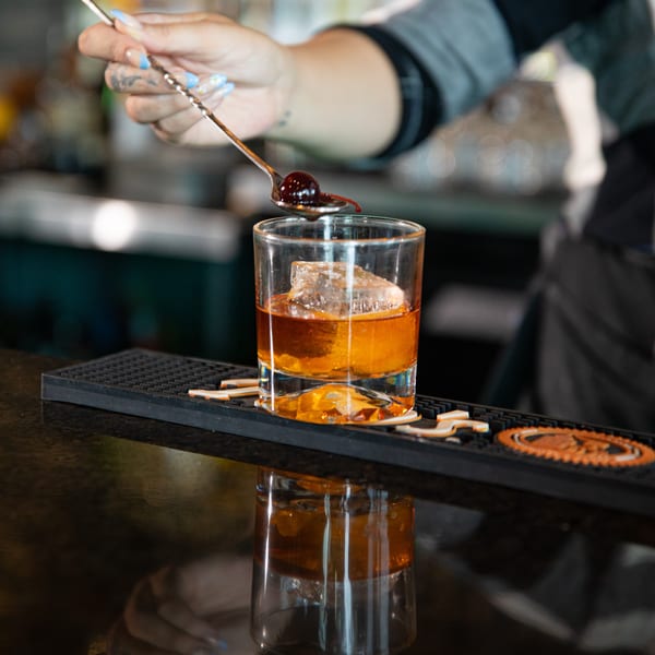 Bartender garnishing an Old Fashioned cocktail with a cherry at The Fields Bar & Grill.