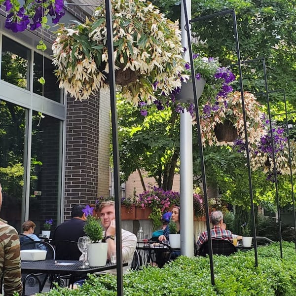 Patrons enjoying the outdoor patio of The Fields Bar & Grill, adorned with hanging flower baskets.