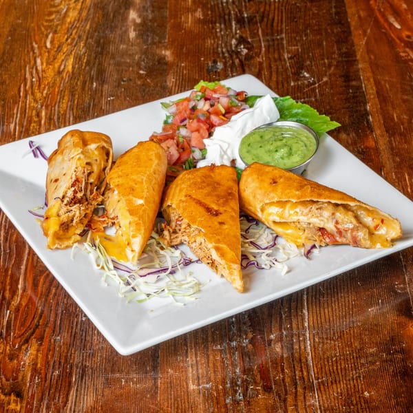 Four golden-brown empanadas filled with chicken and cheese, served with salsa, sour cream, and guacamole.