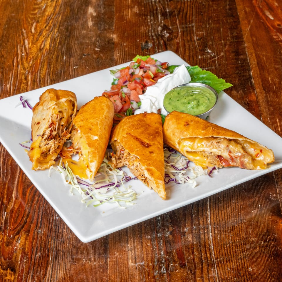Four golden-brown empanadas filled with chicken and cheese, served with salsa, sour cream, and guacamole.