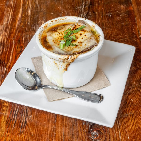 French onion soup in a white crock with melted cheese and green onions, on a wooden table.